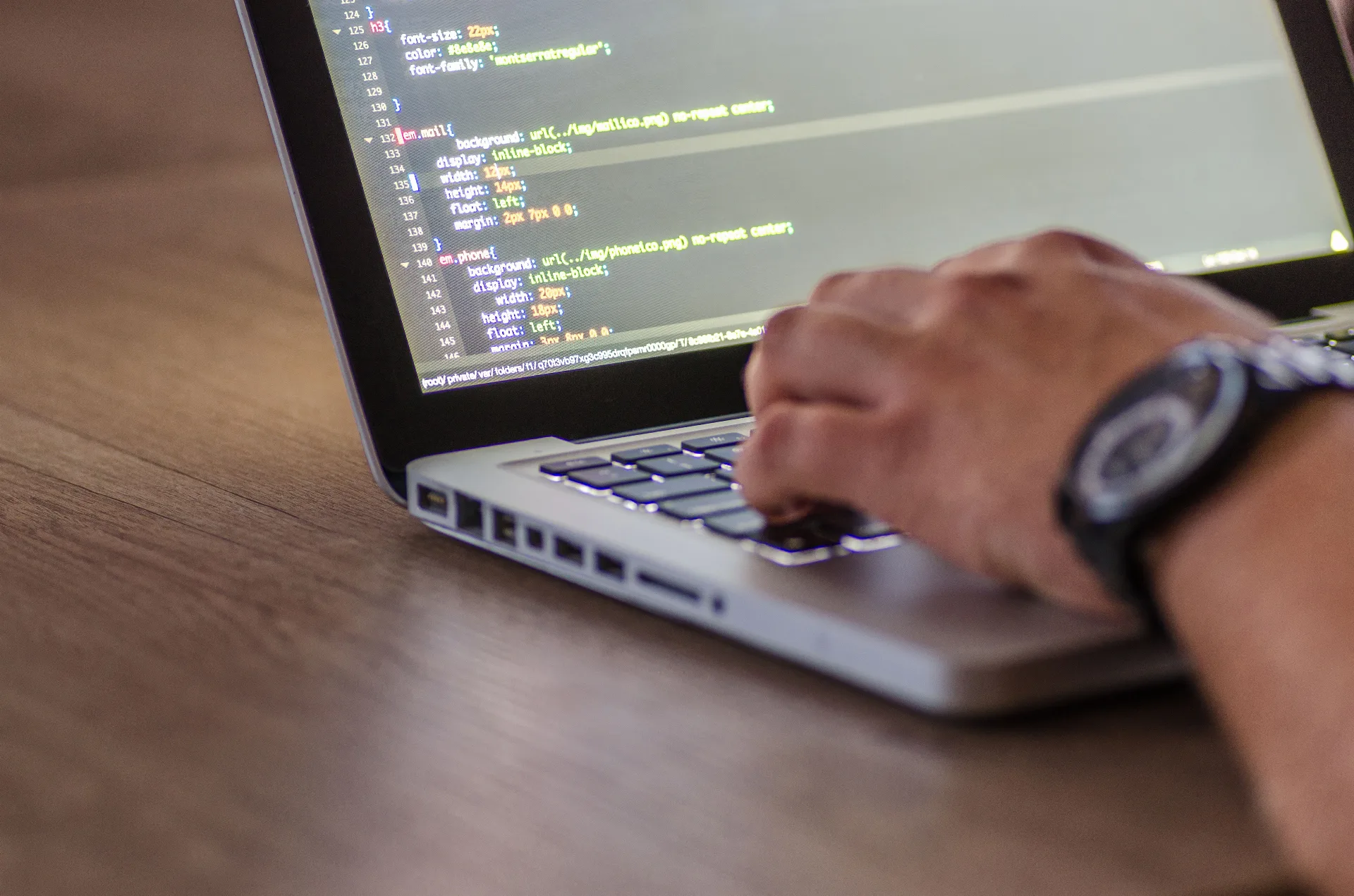 Hände auf der Tastatur eines Notebooks, auf dem Bildschirm CSS-Code