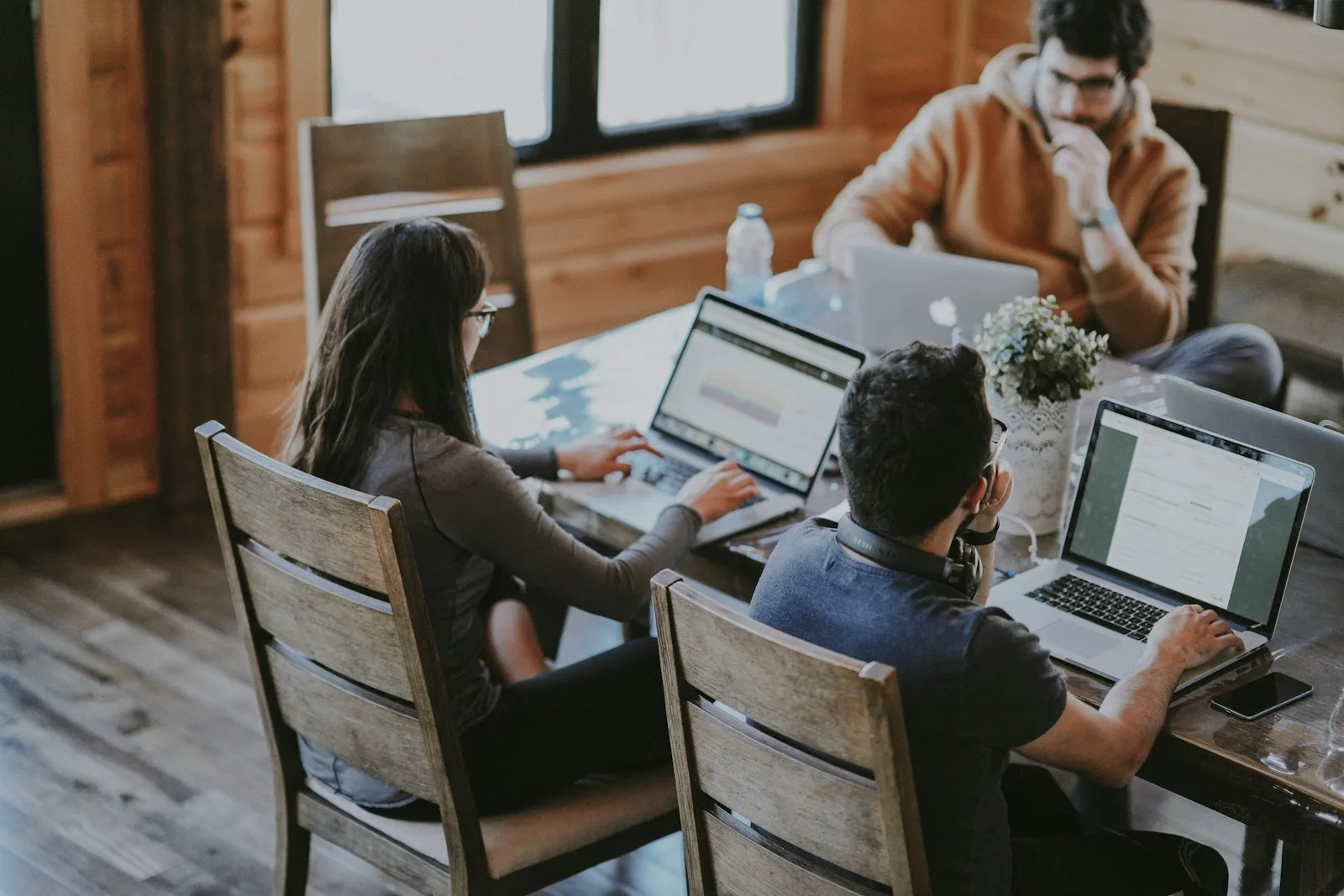 Kleines Team arbeitet gemeinsam an Laptops an einem Holztisch